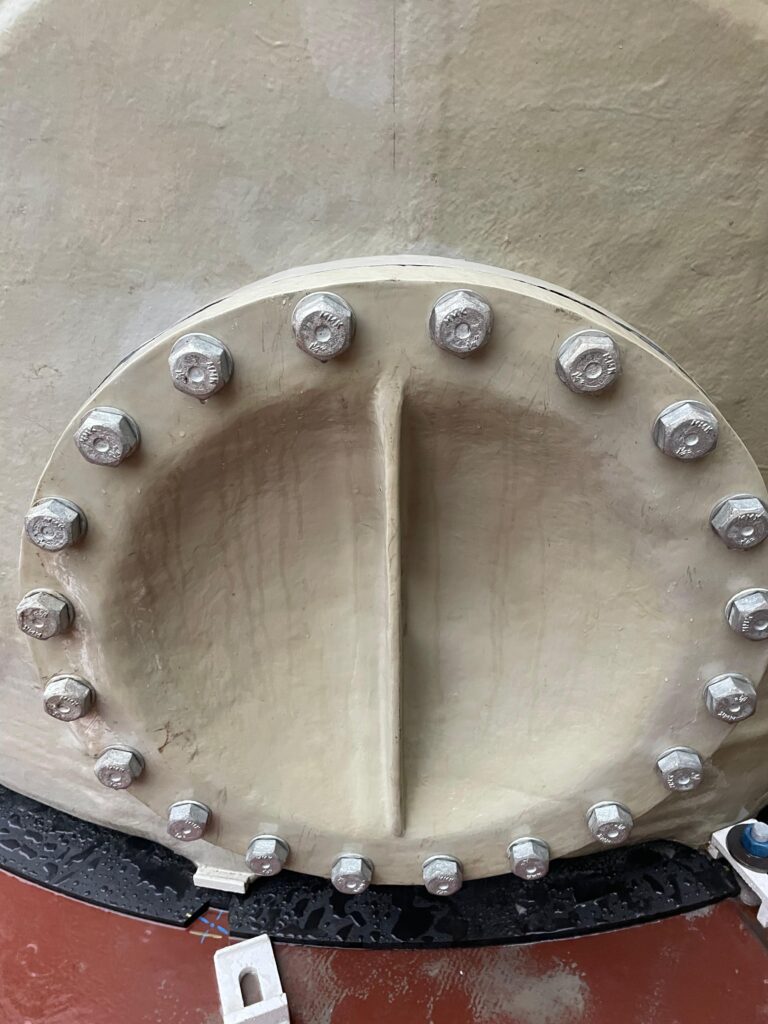 A bolted flanged manway access cover on an industrial FRP chemical storage tank, highlighting a crucial connection point.